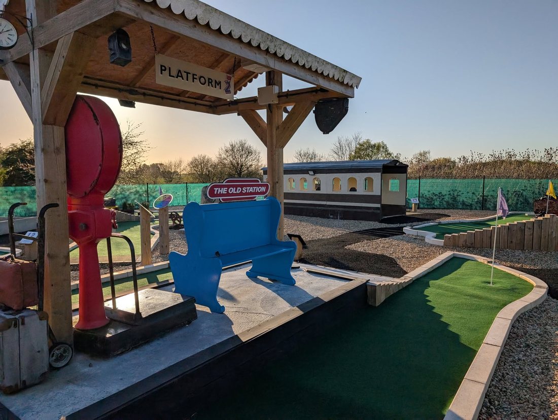 The Old Station hole at Play2Day Wisbech as built, with a timber platform canopy, blue bench, red water crane and a carriage beyond